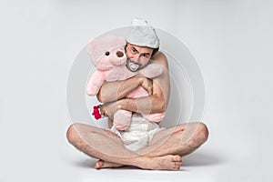 Infant adult man with pacifier in diaper holding pink teddy bear