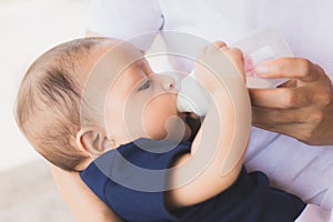 Infant baby on being fed by her mother drinking milk from bottle