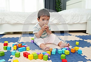 infant baby biting wooden block toy on jigsaw mat in bedroom