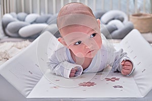 Infant baby boy exercising to keep his head lying on his stomach in the children`s room