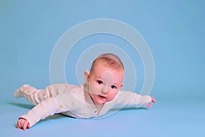 Infant baby boy looks in surprise while lying on his tummy, studio blue background. Four month old child, copy space