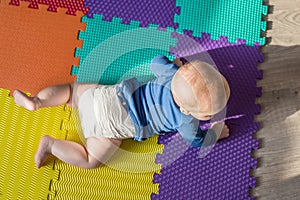 Infant baby boy playing on colorful soft mat. Little child making first crawling steps on floor. Top view from above