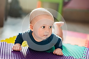 Infant baby boy playing on colorful soft mat. Little child making first crawling steps on floor. Top view from above