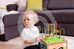 Infant baby boy playing indoors with toy sitting on soft carpet