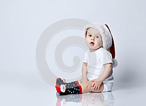 Infant baby boy toddler in christmas socks and cap is sitting on the floor on gray