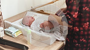 Infant baby on changing table, moving hands and legs, as his mother getting his clothes ready