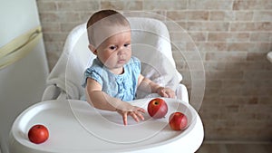 Infant baby eating apple. Cute little girl eating and playing apples in high chair. Adorable child tasting fruit. Healthy eating c