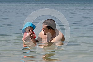 Infant baby girl first time in the sea. She is very impressed and happy. Father holds smiled child in the water and teaches to