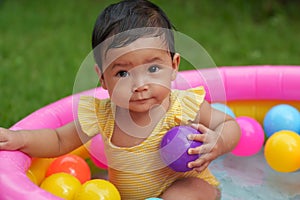infant baby girl playing water with colorful plastic balls in inflatable pool