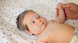 Infant baby girl with surprised face lying on back on blanket, holding hand of father and looking up. Morning exercises for infant