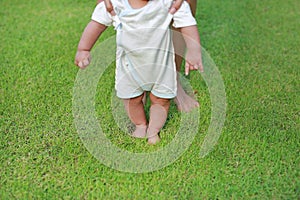 Infant baby learning to walk with his mother on the green grass. First steps