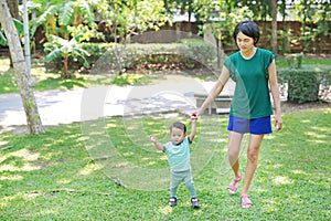 Infant baby learning to walk with his mother on the green grass. First steps