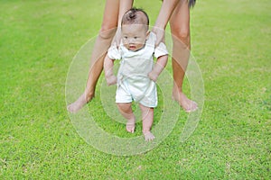 Infant baby learning to walk with his mother on the green grass. First steps