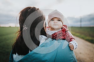 Infant baby looks over mothers shoulder - autumn outdoor family lifestyle concept