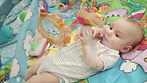 Infant baby playing on colorful mat. Close up of cute baby boy play with toy