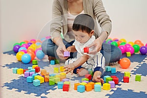 infant baby playing wooden block toy with mother in playpen