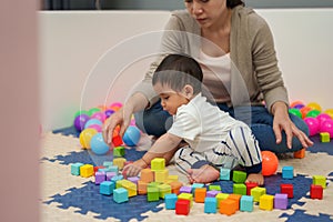 infant baby playing wooden block toy with mother in playpen