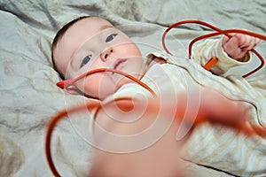 Infant baby plays with a red electric wire and gnaws it with his mouth