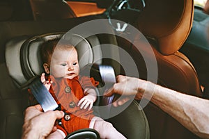 Infant baby in safety car seat and father fastens belt