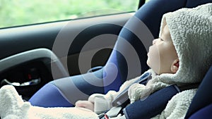 infant baby in white hood sitting blue carseat in driving car, watching window