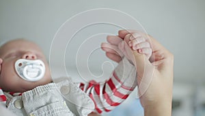 An infant boy with a baby`s dummy holding an adult`s thumb.