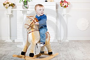 Infant boy in blue sweater and jeans sits on a toy horse. He does not like what is happening. Disgust, loathing