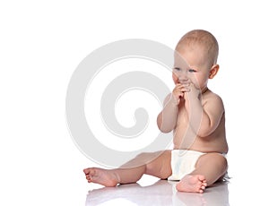 Infant child baby boy in diaper is sitting on the floor holding both his hands in his mouth on white