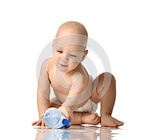 Infant child baby boy toddler sitting in diaper try to take a bottle of water isolated on a white