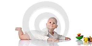 Infant child baby boy toddler in white bodysuit lying on his stomach looking up crawling to get colorful toys on white