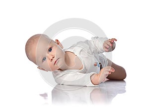 Infant child baby boy toddler in white bodysuit is lying on its side, trying to roll over on white