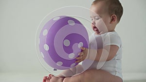 Infant, childhood concept - happy funny playfull toddler kid 8 month baby girl play with purple ballon on birthday party