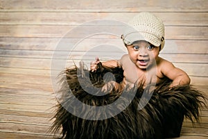 Infant mixed race healthy looking baby boy wearing knitted hat sitting in a fluffy furry basket wooden background modern studio sh