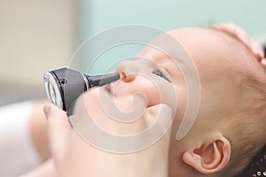 Infant in pediatric clinic. Close-up doctor`s hand with modern otoscope examining baby`s nose. Children healthcare and