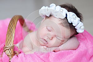 Infant sleeping in basket with accessory - head band, baby girl lying on pink blanket, cute child, newborn