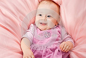 Infant smiling girl relaxing on comforter