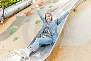 Infantile and happy woman sitting on a kid slide on a playground