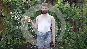 An infantile young man with a beard stands and launches soap bubbles from a toy bubble and tries to catch them with his mouth.