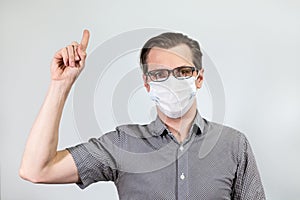 Infected Caucasian man with perfect calm is gesturing with forefinger, pointing with finger upward, grey background