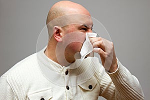 Infected man blowing his nose in tissue paper because of being ill on gray background