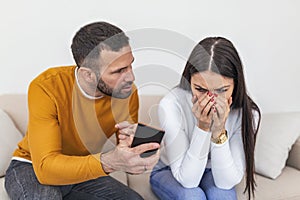 Infidelity. Jealous boyfriend Showing his Cheating girlfriend her Phone Demanding Explanation Sitting On Sofa Indoor. Wife caught