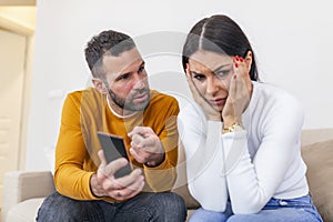 Infidelity. Jealous boyfriend Showing his Cheating girlfriend her Phone Demanding Explanation Sitting On Sofa Indoor. Wife caught