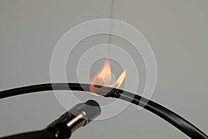Inflamed black wire on grey background, closeup. Electrical short circuit