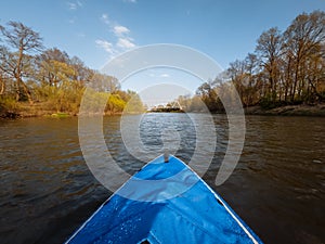 An inflatable blue kayak floats on the river at sunset. View of the bow of the boat