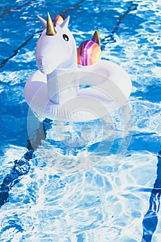 Inflatable colorful white unicorn at the swimming pool. Vacation time in the swim pool with plastic toys. Relaxation and