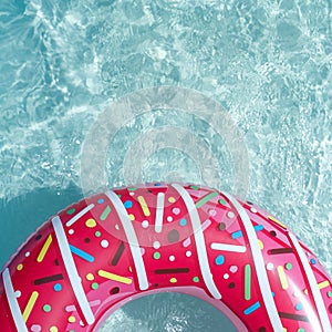 Inflatable float rubber ring in the form of a pink donut in the blue water of the pool