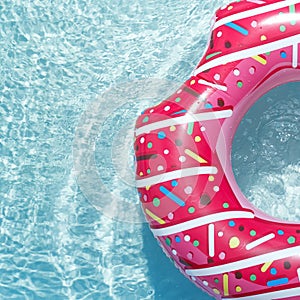 Inflatable float rubber ring in the form of a pink donut in the blue water of the pool