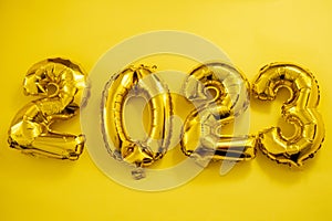 Inflatable golden balloons numbers 2023 on a yellow background. Happy New Year. Flat lay. Copy space. Christmas. Happy
