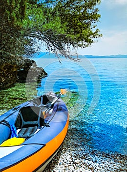 Inflatable kayak in a bay by the sea on a pebble beach. Canoe, sea coast with clear blue water on a sunny bright day in summer