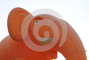 Inflatable pink elephant with white tusks against the blue sky tied ropes