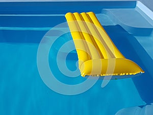 An inflatable yellow mattress floats in a blue pool with clear water. Rest on an artificial reservoir. Relaxation in the spa area